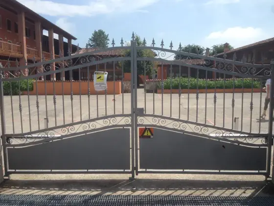 Cancello automatico a due ante battenti in ferro battuto con cartelli di sicurezza
